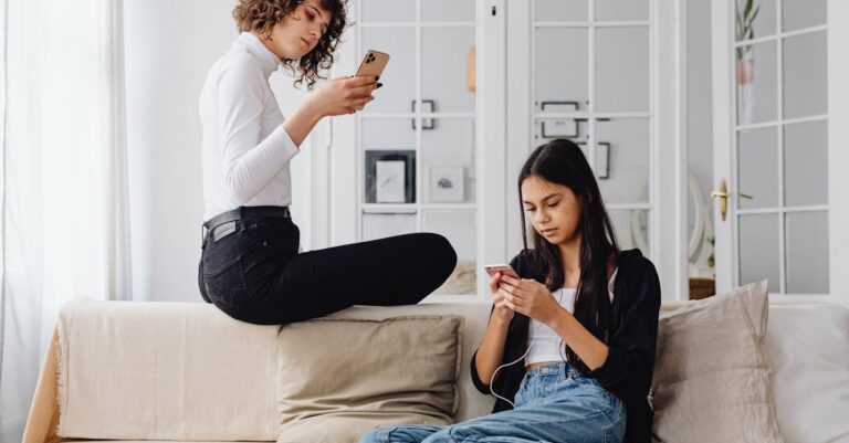 Two women using smartphones while seated on a couch in a modern living room setting.