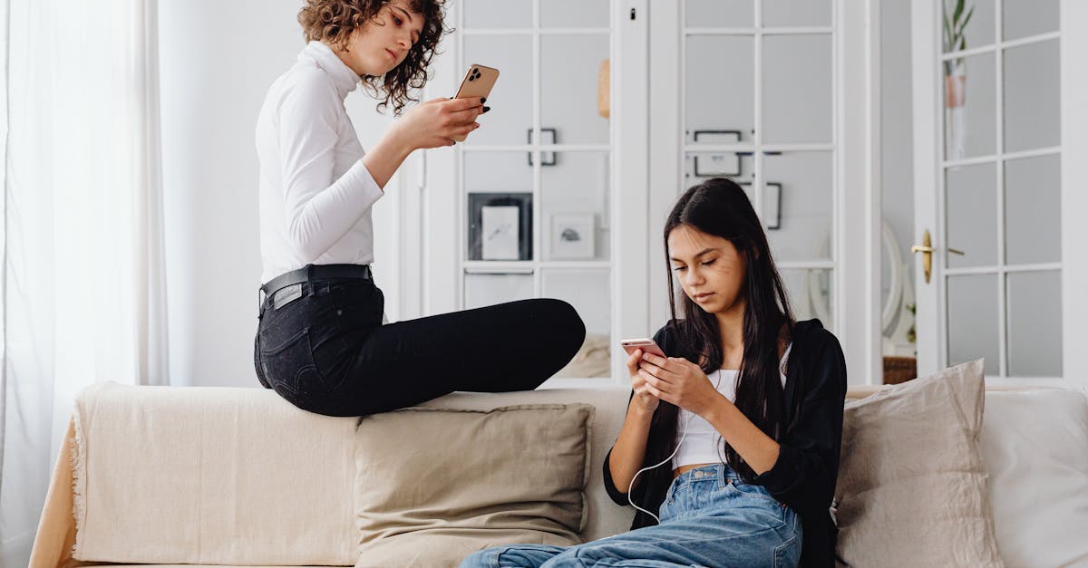 Two women using smartphones while seated on a couch in a modern living room setting.